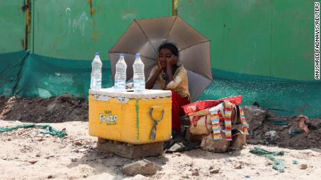 A girl selling water uses an umbrella to protect herself from the sun's rays in New Delhi.