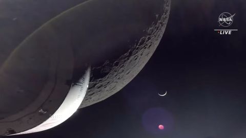 The Orion capsule captures a view of the Moon's surface, with Earth in the background as a crescent moon illuminated by the Sun.